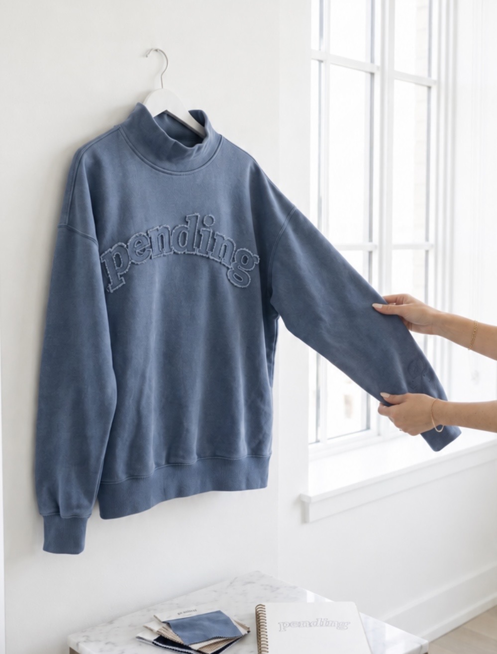 The oversized washed-blue Pending hoodie on a hanger — tall mock neck, arched pending appliqué, no front pocket